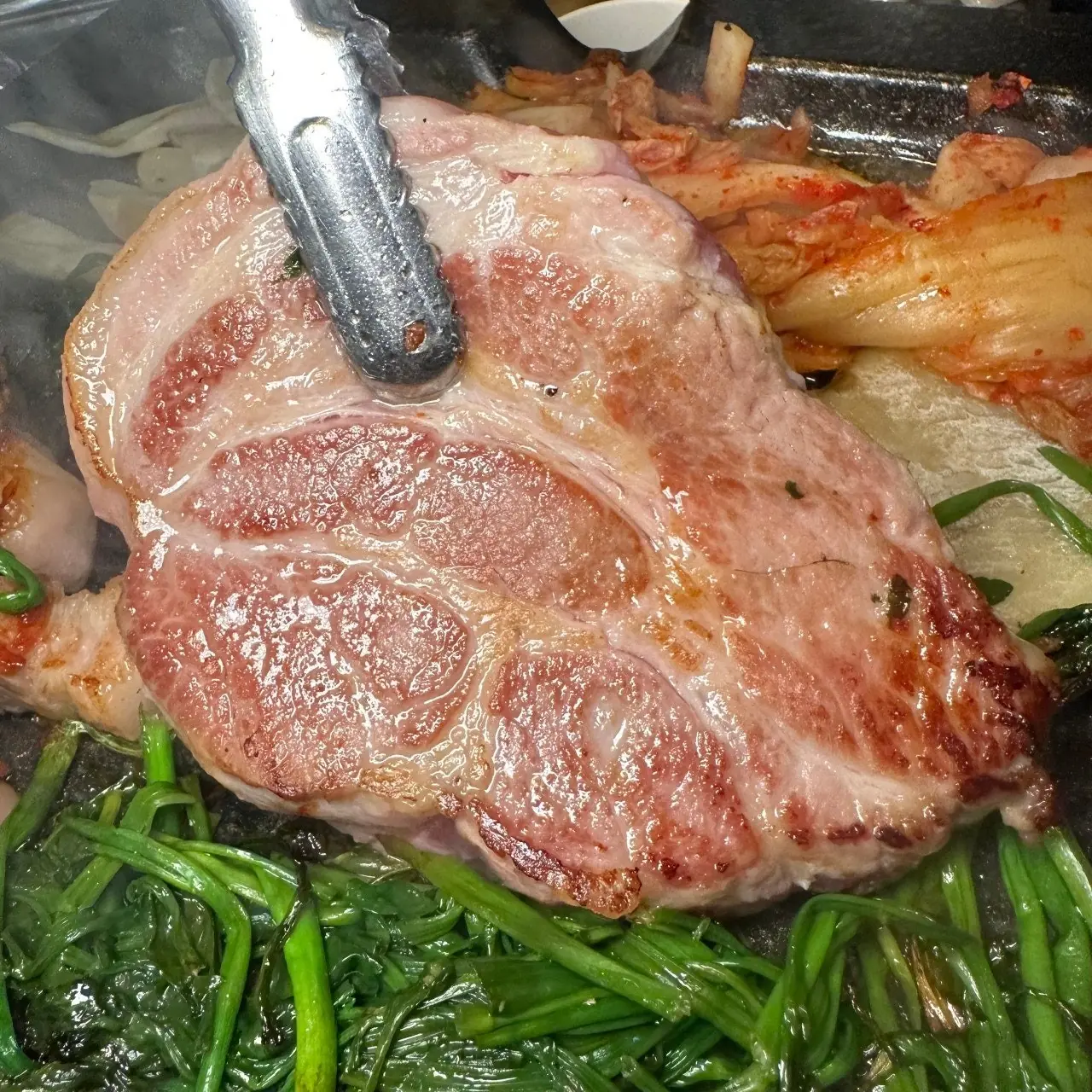불판 위에서 구워지는 김숙성 홍대점 두툼한 특목살과 미나리 — thick-cut aged pork neck grilling with minari at Kim Sukseong Hongdae Korean BBQ